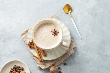 Traditional Indian masala chai tea with milk and spices in a white cup on a light blue background with spoon.