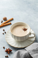 Traditional Indian masala chai tea with milk and spices in a white cup on a light background with napkin.