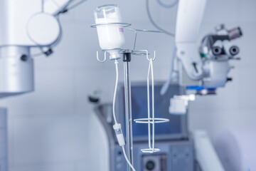 IV infusion bottle and ophthalmic operating room with surgical microscope background