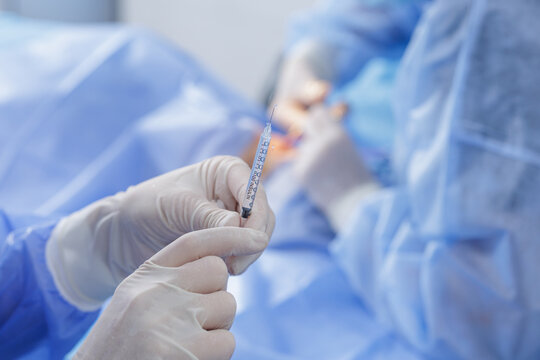 Gloved clinician priming fine syringe for local anesthesia in a sterile operating room