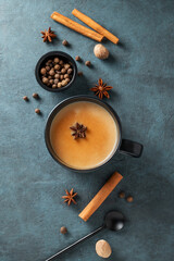 Traditional Indian masala chai tea with milk and spices in a black cup on a dark background with...