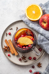 A cup of red mulled wine with spices, orange and apple slices on a light background