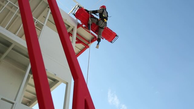 Rescue workers prepare for rappelling practice on a specialized high angle training tower, featuring a climbing wall against a bright sky, emphasizing readiness and skill development.