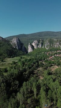 Aerial view of Jerma Canyon in Serbia with a small village surrounded by rocky cliffs and green forest. Vertical 4k footage