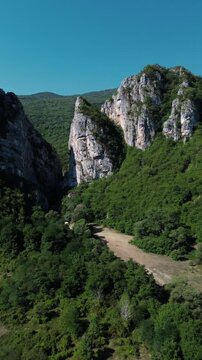 Aerial view of Jerma Canyon in Serbia with a small village surrounded by rocky cliffs and green forest. Vertical 4k footage