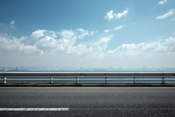A modern bridge road overlooking a distant city skyline under a bright blue sky with soft clouds, ideal for automotive and travel advertising backgrounds.