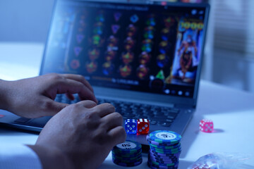 Close-up of a man's hands playing online slot gambling in front of a laptop with a stack of dice and poker chips, ready to express his victory. The concept of gambling. Winning and losing in gambling.