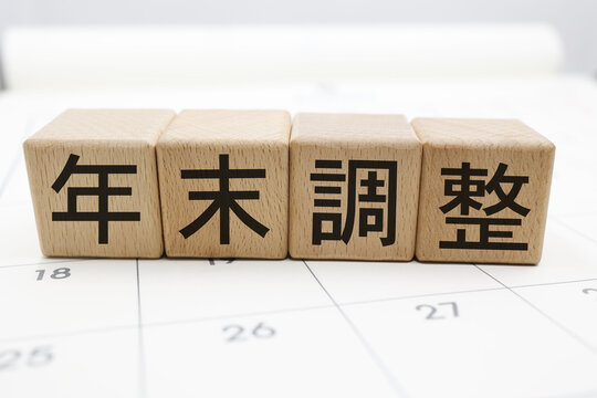 カレンダー背景に並ぶ木のブロックと年末調整の文字イメージ。