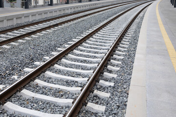 Fototapeta premium Railway tracks with gravel bed and concrete ties, curving gently along the platform, showcasing the infrastructure of modern transportation systems