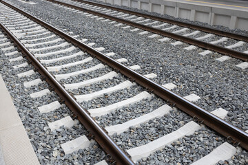 Railroad tracks with gravel bed, featuring parallel steel rails and concrete ties, creating a strong visual of transportation infrastructure and engineering design