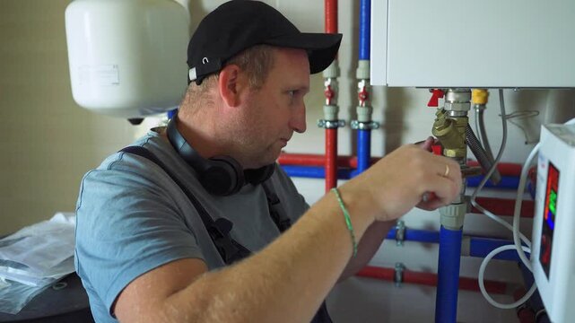 Accident, breakdown in heating system. Plumber is repairing boiler. Maintenance worker is tightening nut onto water pipe with wrench. Break in pipe supplying water, antifreeze to home's heating system