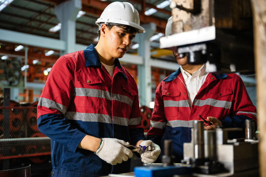 Engineering instructor guiding apprentice in machine operation during industrial training at manufacturing plant. Engineers and technicians working together in a factory inspecting machinery.