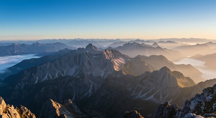 Panoramic view of majestic mountain range at sunrise with misty valleys and clear sky.