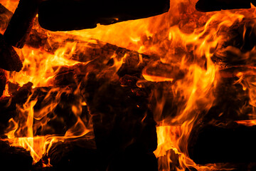 Narrow focus of a crackling bonfire at night in Brazil. Orange flames dance among stacked wood,...