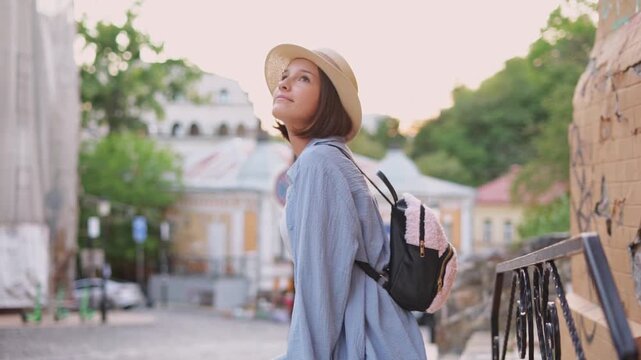 Cute young tourist girl in straw hat with backpack sitting on open terrace in tourist city enjoying travel and vacation rest