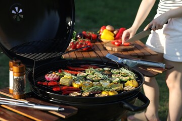 Vegetarian barbeque. Woman cutting products at table outdoors, focus on grill with cooked vegetables