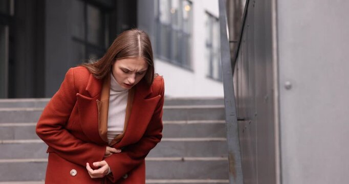 Young woman suffering from stomach ache and nausea outdoors. Camera tracking