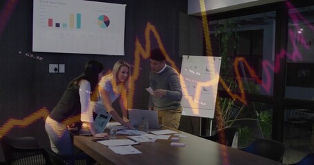 Three colleagues reviewing reports and charts in meeting room with screen, flipchart and laptop