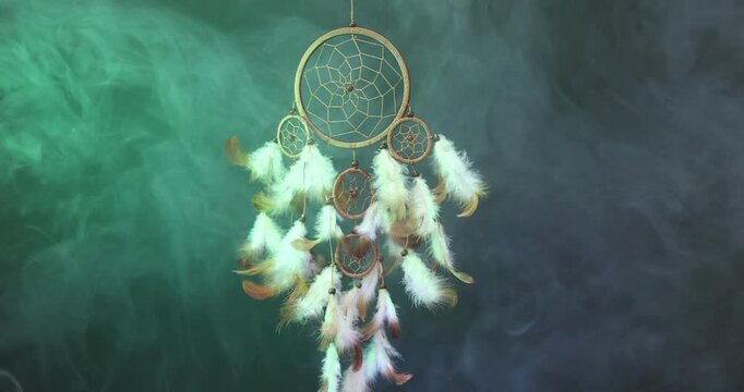 Beautiful dream catcher and smoke flowing in color light on dark background