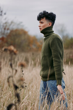 A candid portrait of a lone model standing in tall grass, wearing a forest green knit turtleneck, conveying authenticity and quiet realism in natural light.