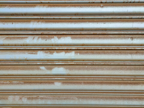 The image shows a weathered, metallic roller shutter door, also known as a roll up door