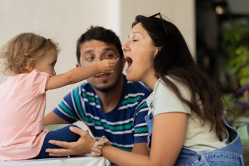 Young child feeding mother while father watches at a casual family meal outdoors