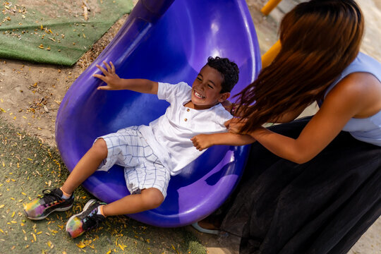 Mother and son playing on a playground slide on a sunny day