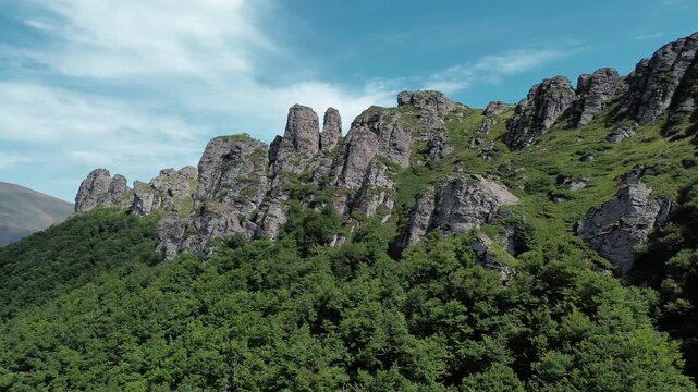 Rocky peaks of Babin Zub mountain in Stara Planina National Park, Serbia, rise above green forests under a blue sky. Aerial view from drone. Horizontal 4k footage