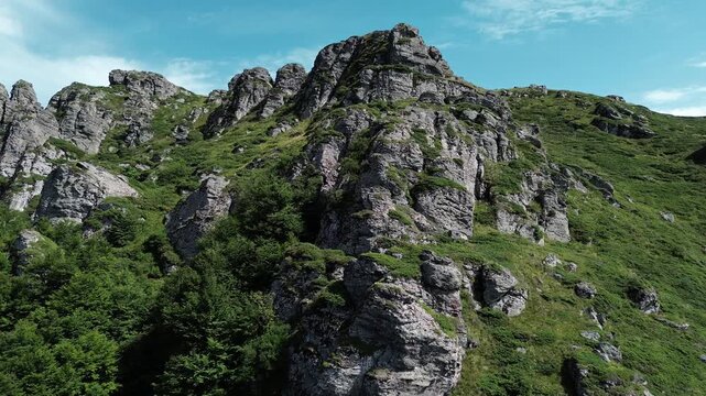 Rocky peaks of Babin Zub mountain in Stara Planina National Park, Serbia, rise above green forests under a blue sky. Aerial view from drone. Horizontal 4k footage
