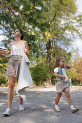 Mother and daughter walking together in a sunny park with greenery
