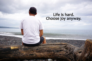Words of wisdom - Life is hard. Choose joy anyway. With a man sitting on a long log wood from behind in the beach. Life inspirational. Happiness quotes.