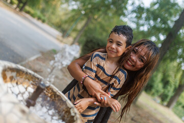 Mother and son enjoying outdoor fun by a fountain on a sunny day