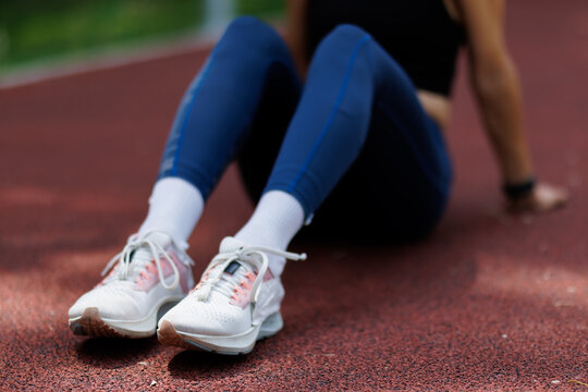 Close-up of an athlete resting on a track wearing stylish running shoes and blue leggings