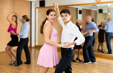 Naklejka premium Cheerful young couple practicing passionate samba in dance class. Amateur dancing concept..