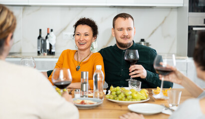 Couple are sitting at table with friends, drinking wine and enjoying snacks, chatting merrily, raise glass to, celebrating important event.