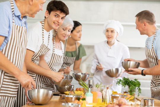 Young female chef at master class teaches group of people how to cook food - Powered by Adobe
