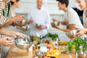 Metal bowl with sauce mixed by young woman's hands holding whisk during cooking classes