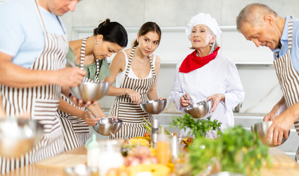 Amiable senior woman, qualified chef, running culinary courses for mixed age group of ordinary people, sharing secrets of cooking .. - Powered by Adobe