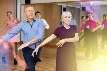 Obraz premium Cheerful elderly woman and man enjoying active dancing in pair during group training in dance studio, practicing playful jitterbug moves