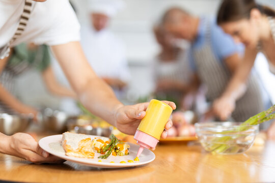 Hands of aspiring cook garnishing and seasoning finished fish dish with sauce, preparing for presentation. Concept of mastering skills in cooking courses..