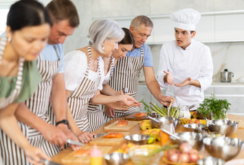 Serious young man chef of cooking course teaching attendees how to cook salmon fish