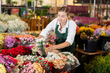 Female employee uses carnation flowers to create bouquet. Flower megamarket, potted and cut flowers, gardening ideas, gardening supplies.