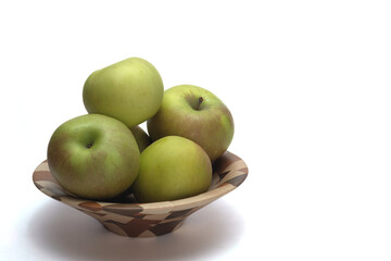 Green apples in a wooden bowl.  The apples are in left frame. The subject is on a white background with ample space for text. 