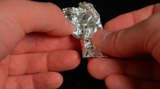 Hands of the person at the party or dance club open or tear foil with LSD strip blotter with dry drop of Lysergic acid drug, lucy, or Ellis D. Hallucinogenic drug in the foil for consumption.
