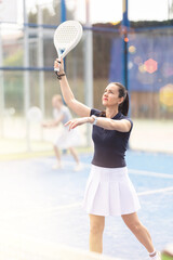 Adult woman playing doubles padel tennis with female partner on court