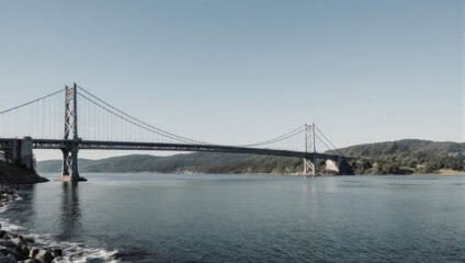 Fototapeta premium A long suspension bridge spans a body of water, connecting landmasses under a clear blue sky