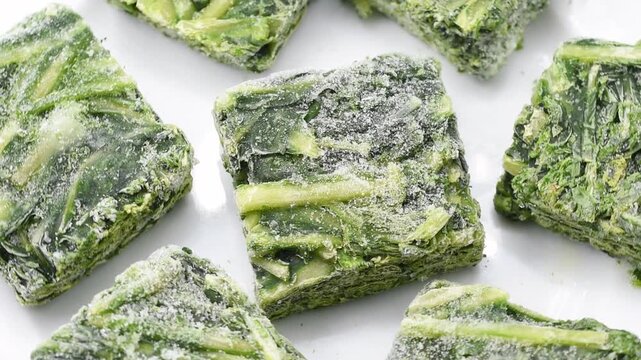 Close-up of frozen chicory Catalogna cubes, showing frosty green leaves and icy texture, representing fresh preserved Italian vegetable for cooking and healthy frozen food concept.Rotating video.