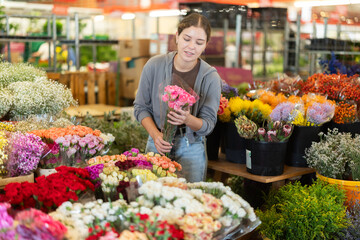 Near showcase with cut flowers, girl visitor examines bunches of carnation, selects flowers, and buys bouquet at self-service store...