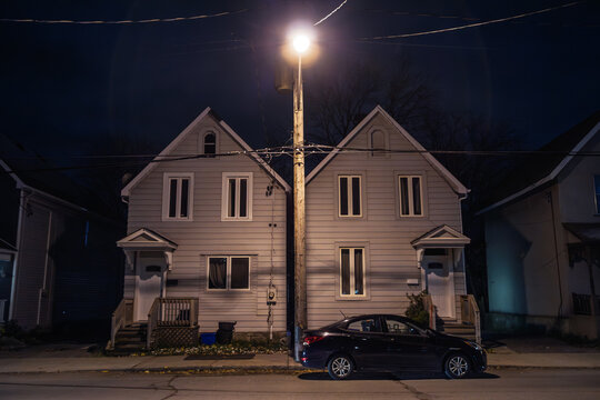 Typical North American wooden houses line a quiet residential street in Ottawa, Ontario. Night lighting, gabled roofs create a symmetrical autumn scene of suburban architecture.