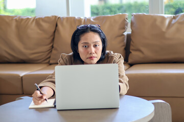 Naklejka premium Asian woman sitting on the floor with laptop on table taking notes in notebook, working from home, workspace